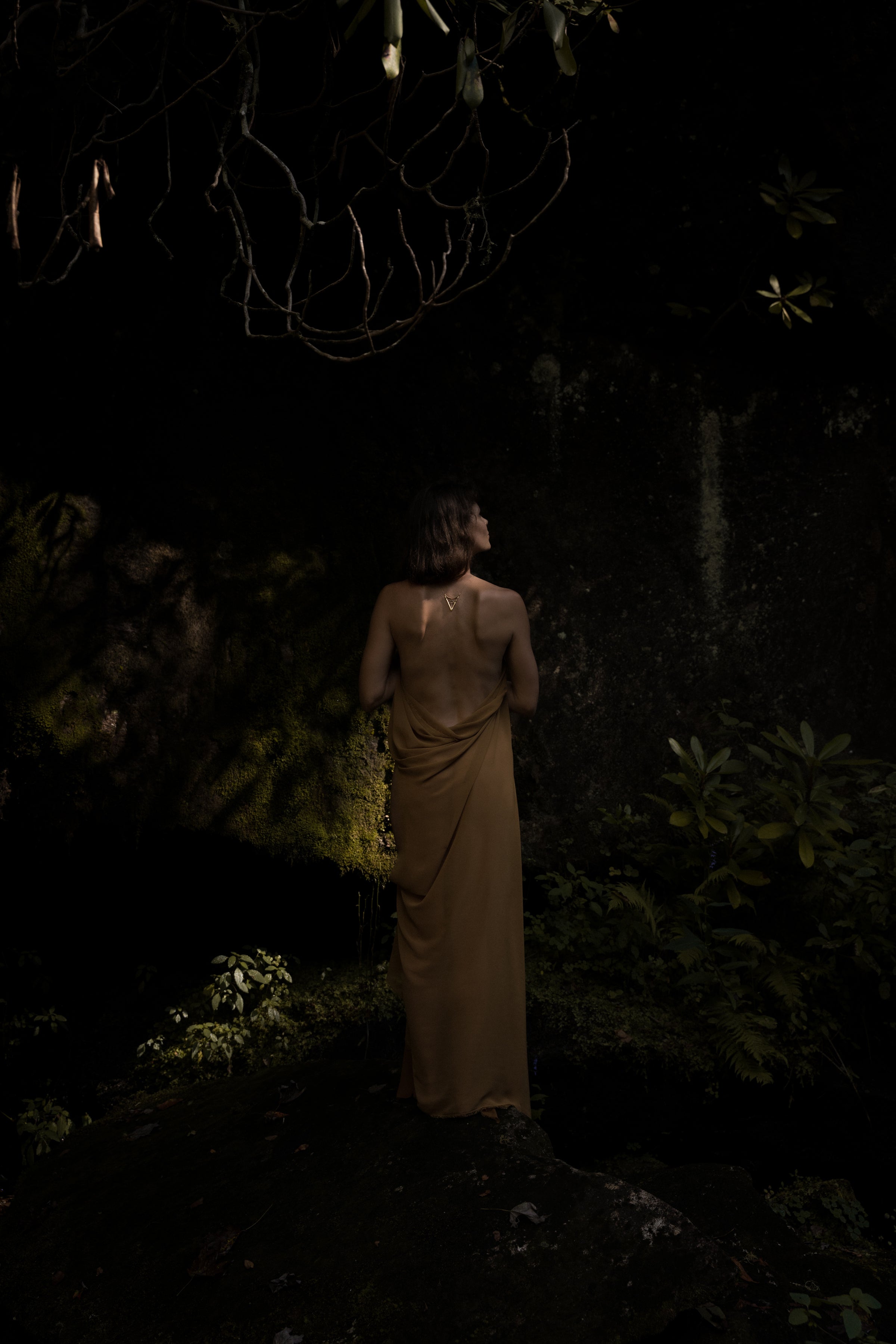 Woman in a long, light-colored dress standing in a dark forest