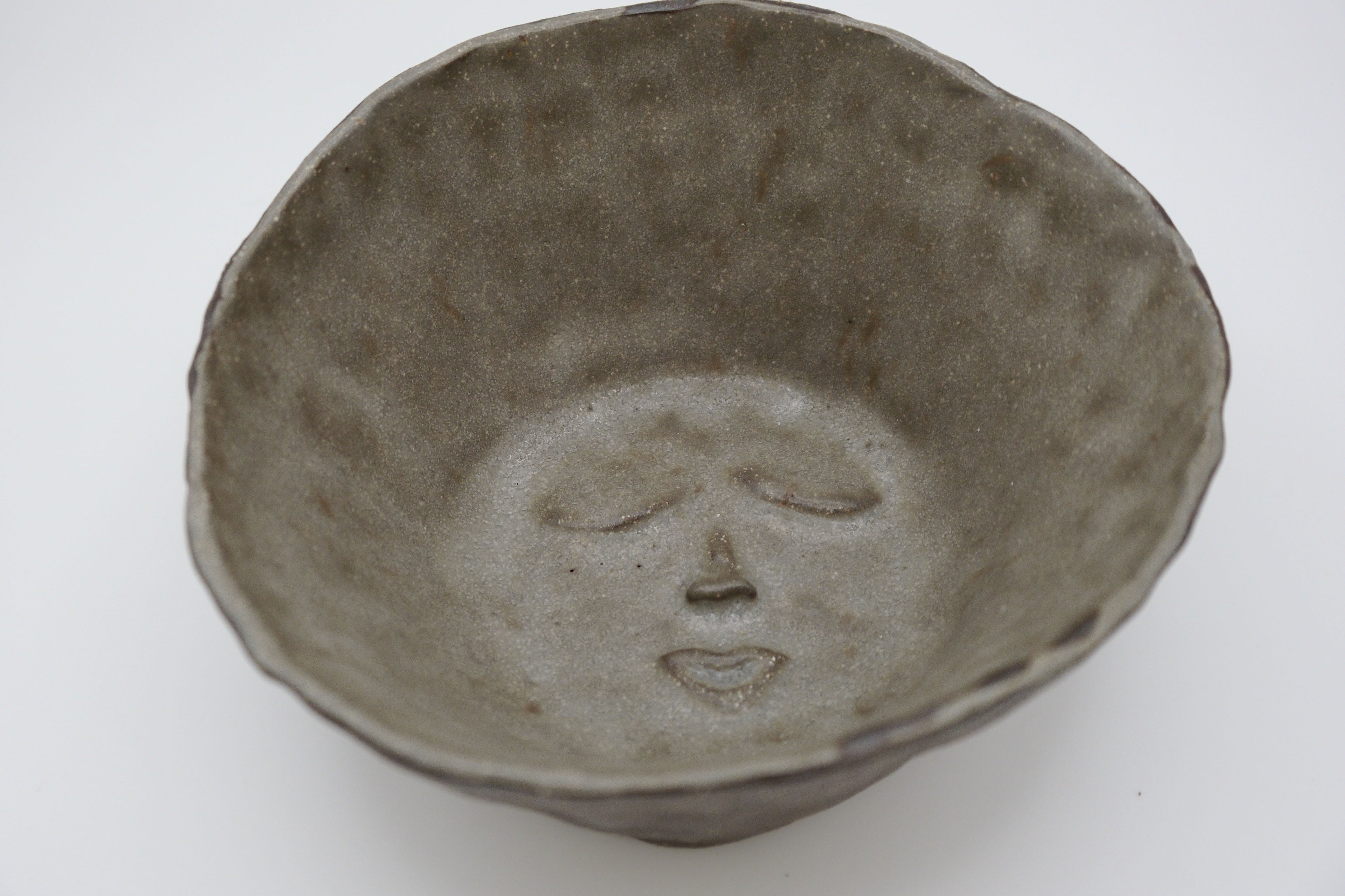 Black clay ceramic bowl with a face design on a white background